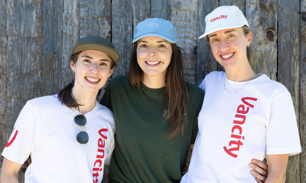 Three women in Vancity and FCU Community Financial t-shirts stand smiling arm in arm.